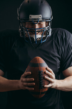 American football player in black sportwear with a ball on black backgroundの写真素材