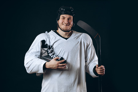 Confident hockey player looking at camera with skate in hand. Isolated on black.の写真素材