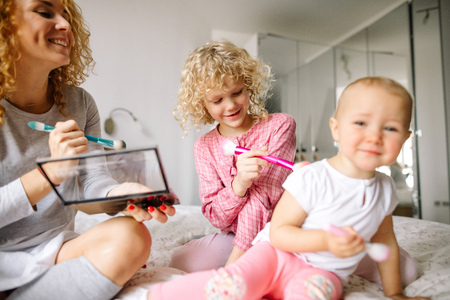 cheerful red-haired woman and her daughter tickling the baby with brushesの写真素材