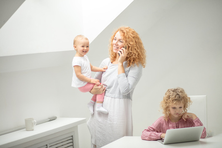 attractive woman gossiping on the phone while her child sitting at the laptopの写真素材