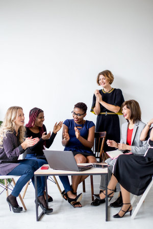 Positive women discuss organization plan while sitting at the table with laptopの写真素材