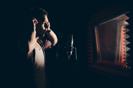 talented man in headphones singing his own song in the dark studioの写真素材