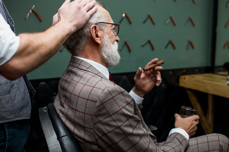 Bearded old businessman sitting at barber shop in chair choosing haircut designの写真素材
