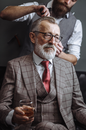 Bearded old businessman sitting at barber shop in chair choosing haircut designの写真素材