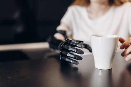 disabled girl controlling her actitions, close up cropped photo. artificial fingers touching the cup on the table, sensorics conceptの写真素材
