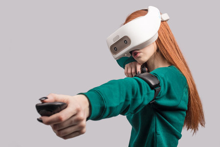 Active beautiful female player with long red hair , being excited watching virtual reality play with...