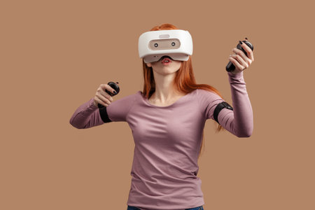 Casual ginger-haired woman in purple pullower wearing VR headset and looking involved in 3D...