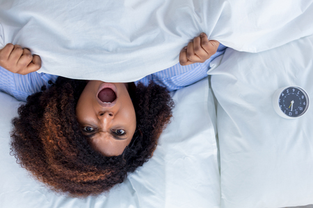 Scared woman lying in bed. top view photo.angry girl hates her noisy neighboursの写真素材