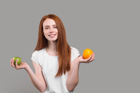 Beautiful young woman holding an apple and a orange in the studio, vitamin, health care, copy spaceの写真素材