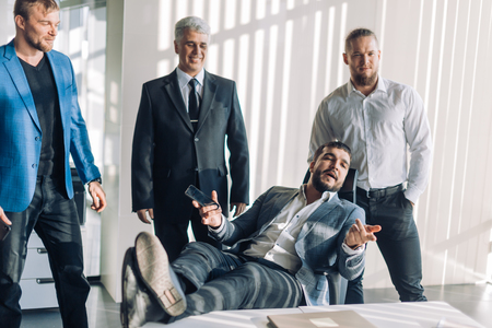Impressive satisfied happy confident executive in suit sitting at chair at meeting table looking at camera with business partners team at backgroundの写真素材