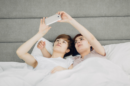 pleasant awesome girls makes while laying in a bedroom. free time, spare time, lifestyle, girls testing anew cameraの写真素材