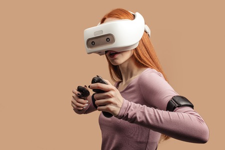Emotional female with red long hair standing experiencing vertual reality headset for the first time. Generation of realistic images of alternative digital realityの写真素材