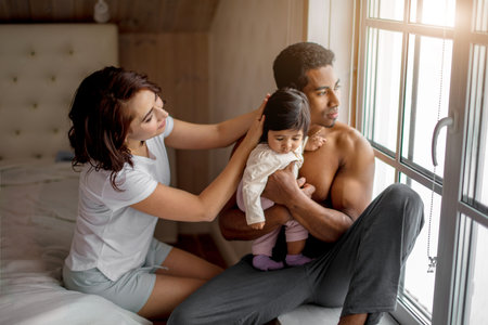 brutal muscular pensive daddy holding his little child and looking at the window while mother...