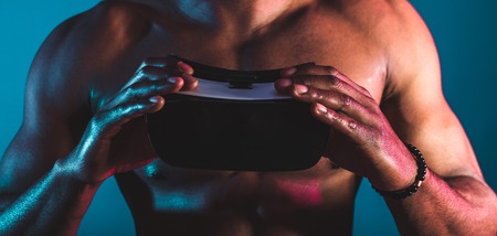 People, technology, sport and cyberspace concept. Cropped shot of African man holding goggles or oculus, experiencing virtual reality, playing video gameの写真素材