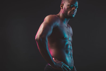 Attractive African male fighter or boxer posing shirtless, looking at camera, isolated over dark background. Awesome young bodybuilder.の写真素材