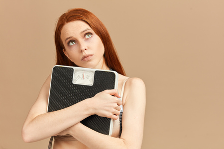 Beautiful young woman holding scale, looking upの写真素材