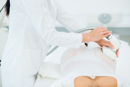 Young brunette female therapist doing beauty therapy against cellulite with LPG machine on woman s buttocks in health and wellness medical clinic. LPG massage for lifting bodyの写真素材