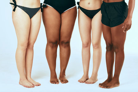 Bare legs of four happy diverse multiethnic women in swimsuits isolated on white