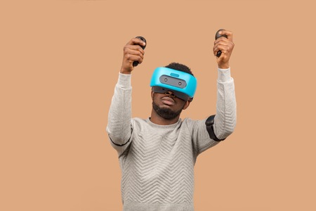 Virtual reality technology is constantly making huge advances. African casually dressed man trying on VR glasses isolated over beige backgroundの写真素材