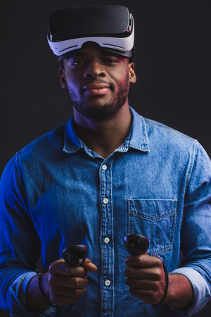 3d technology, virtual reality, gaming, entertainment and people concept - confident dark skinned man taking off virtual reality headset or 3d glasses while playing game over black backgroundの写真素材
