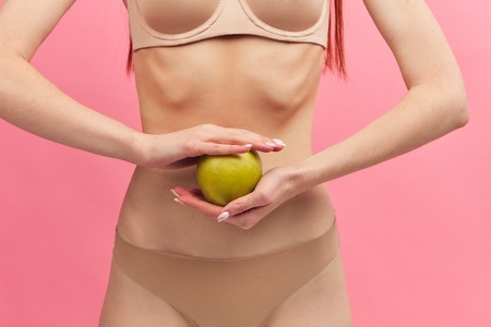 Midsection portrait of female thin skinny body in nude underwear, holding green apple for wellness, weight loss and healthy isolated on pink background, healthcare and diet concept.の写真素材