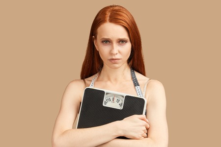 Diet and weight, young woman holding scales in hands feeling sad and depressed, lの写真素材
