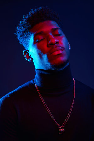 Handsome young African man with glasses and dressed in poloneck sweater standing with closed eyes on...