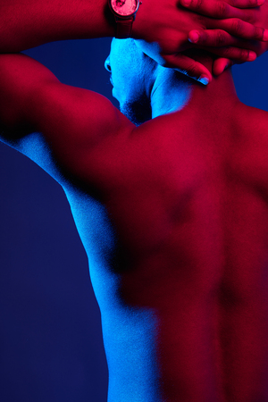 Rear view of African male athlete with naked back posing against dark purple wall. Low key photo.の写真素材