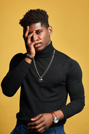 Grieved depressed sad young dark-skinned man having some problems with health or private life. Isolated studio shot of tired african man keeping hand on forehead and looking at camera on dark wallの写真素材