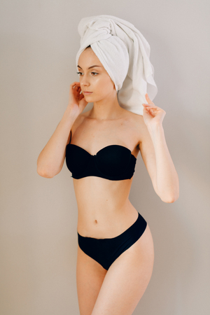 Portrait of beautiful young woman in black lingerie posing with towel on head over light backgroundの写真素材