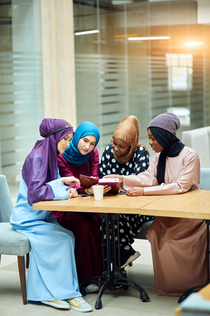 Photo of a happy young multiethnic arabian business women dressed in hijab reading book in modern cafe.の写真素材