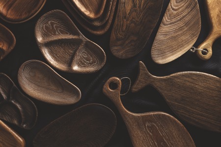 Top view of unused brand new brown handmade wooden kitchen utensil, made from different wood species, dish plate and cutting board on black backgroundの写真素材