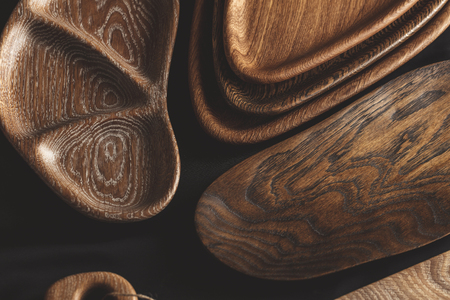 Top view of unused brand new brown handmade wooden kitchen utensil, made from different wood species, dish plate and cutting board on black backgroundの写真素材