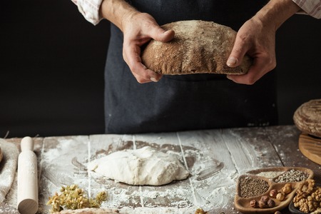 Hands of undentified baker man in cooking wear, holding homemade sourdough bread, food conceptの写真素材