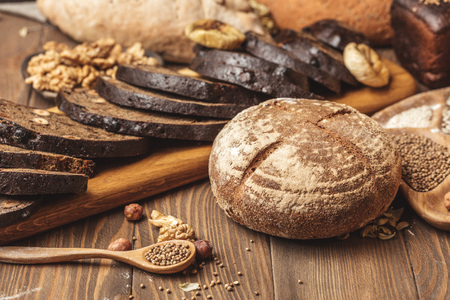 Whole grain, whole loaf and sliced pieces of multigrain bread contains whole grains ( poppy, millet, flaxseed, pumpkin seeds, and sunflower seeds) isolated on dark wooden table .の写真素材