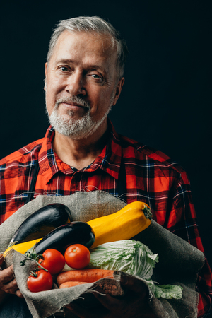 handsome senior gardener with fresh autum vegetables. close up photo. studio shot. isolated black background.food ,farmingの写真素材