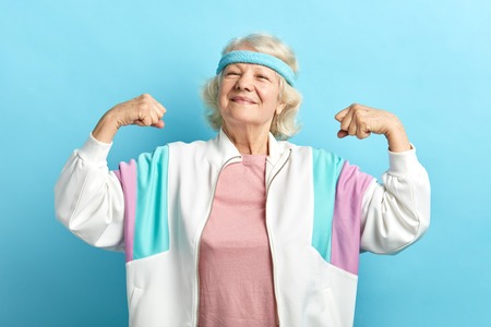 Happy, proud elderly attractive woman flexing both arms in the air with fists pressed showing strength or success, celebrating sport achievements.の写真素材