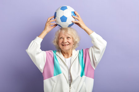 Happy senior female football player in sportswear keeping football on head, enjoying a goal scored...