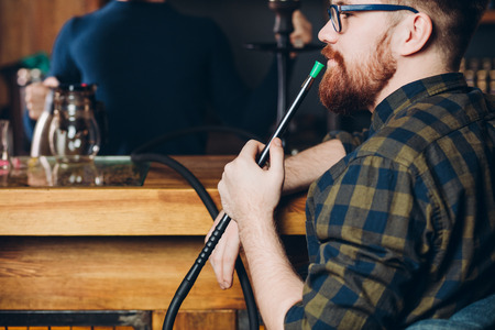 The red-haired pensive guy smokes. Steam from the hoockah.close up side view photo. free time. hobby. spare timeの写真素材