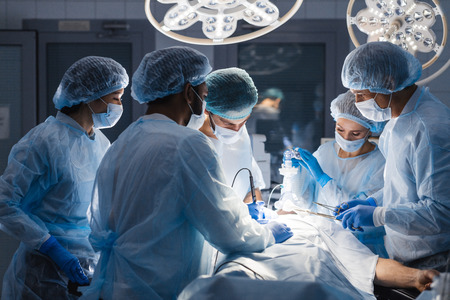 Group of concentrated surgeons engaging in rescue of male patient in operation room at hospital, emergency case, surgery, medical technology, health care and disease treatment conceptの写真素材