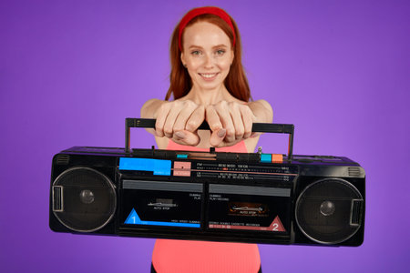 cropped shot of female aerobics trainer stands with hands forward holding portable stereo cassette...