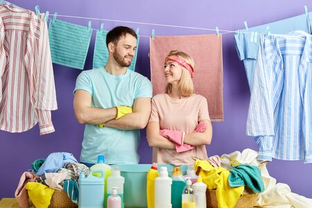 awesome positive couples with folded arms looking at each other. close up photo. household chores, clean wet clothes hanging on the clothespins. blue background. studio shot.free time, spare timeの写真素材