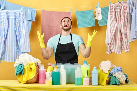 angry man in apron shouting and looking up. close up portrait. guy in blue T-shirt is angry as hehas used bad detergent. man has problems, cannot choose the washing liquid.の写真素材