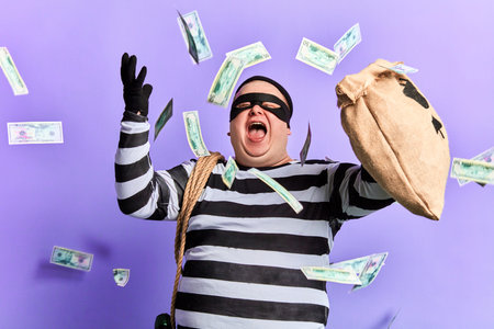 happy cheerful thief enjoying stolen money. isolated blue background studio shot. emotion and...