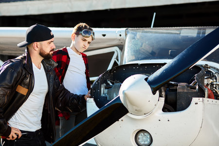 father and son standing together, looking at light propeller airplane engine thoughtfully, searching for reason of breakdown, going to fix the mechanism. Aviation concept.の写真素材