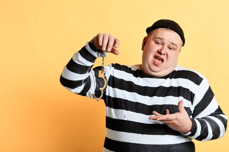 piece of cake, fat plump criminal showing broken handcuff and looking at camera. isolated yellow background. studio shot.の写真素材
