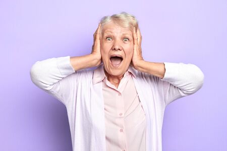 emotional lady in blouse and shirt keeps hands on face screaming, as she has won the lottery, car, house . success, close up portrait, isolated light blue background. studio shotの写真素材