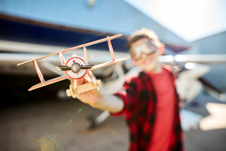 close up view of model propeller plane, blurred shot of little boy playing with the toy near hangar...