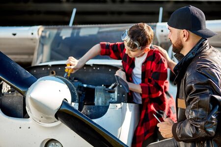 close up view of dad and son doing repair works for light propeller airplane, brought instruments to hangar, fixing gear mechanism together, holding screwdriver and pliers.の写真素材