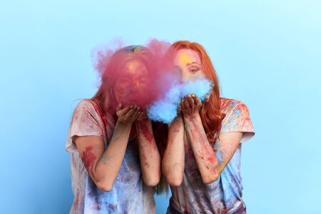 happy funny girls blowing colourful powder during the holi festival. close up photo. isolated blue background, studio shot.magic time.の写真素材